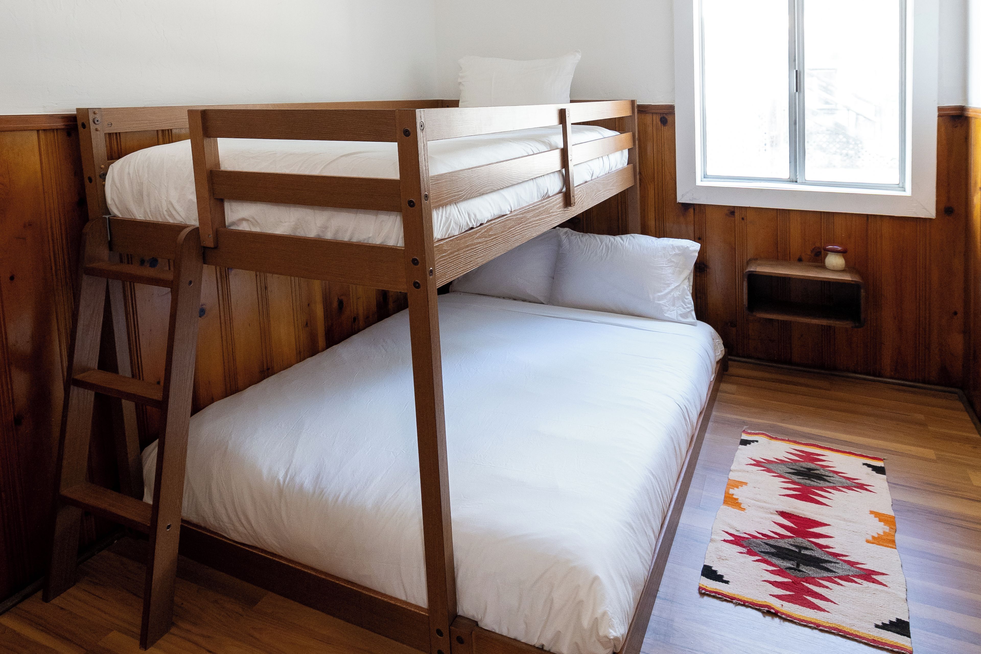 Een slaapkamer met een stapelbed, een raam, houten wanden en een vloerkleed.