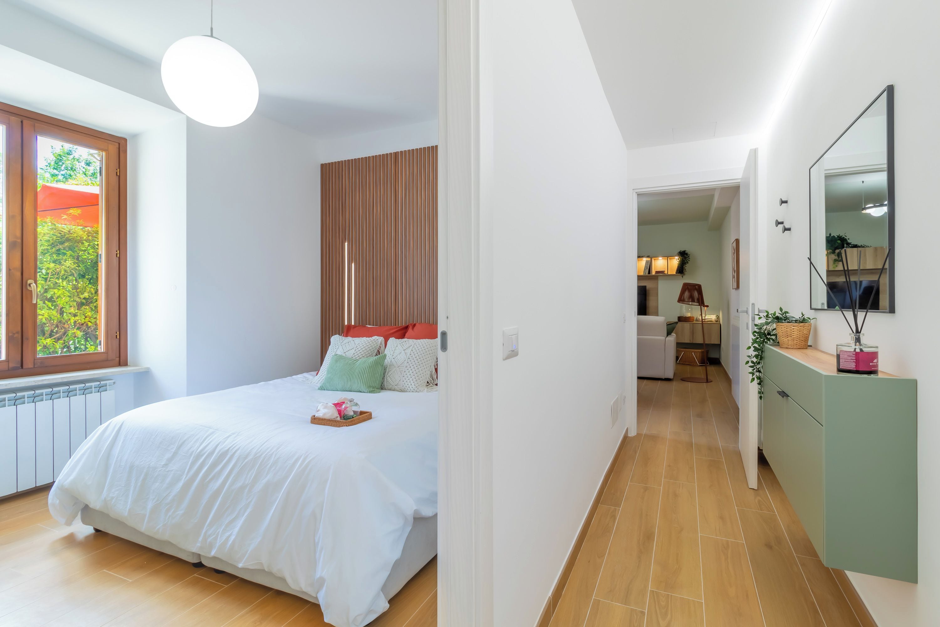 A bedroom with a bed, a bedside table, a window, and a view of a garden.