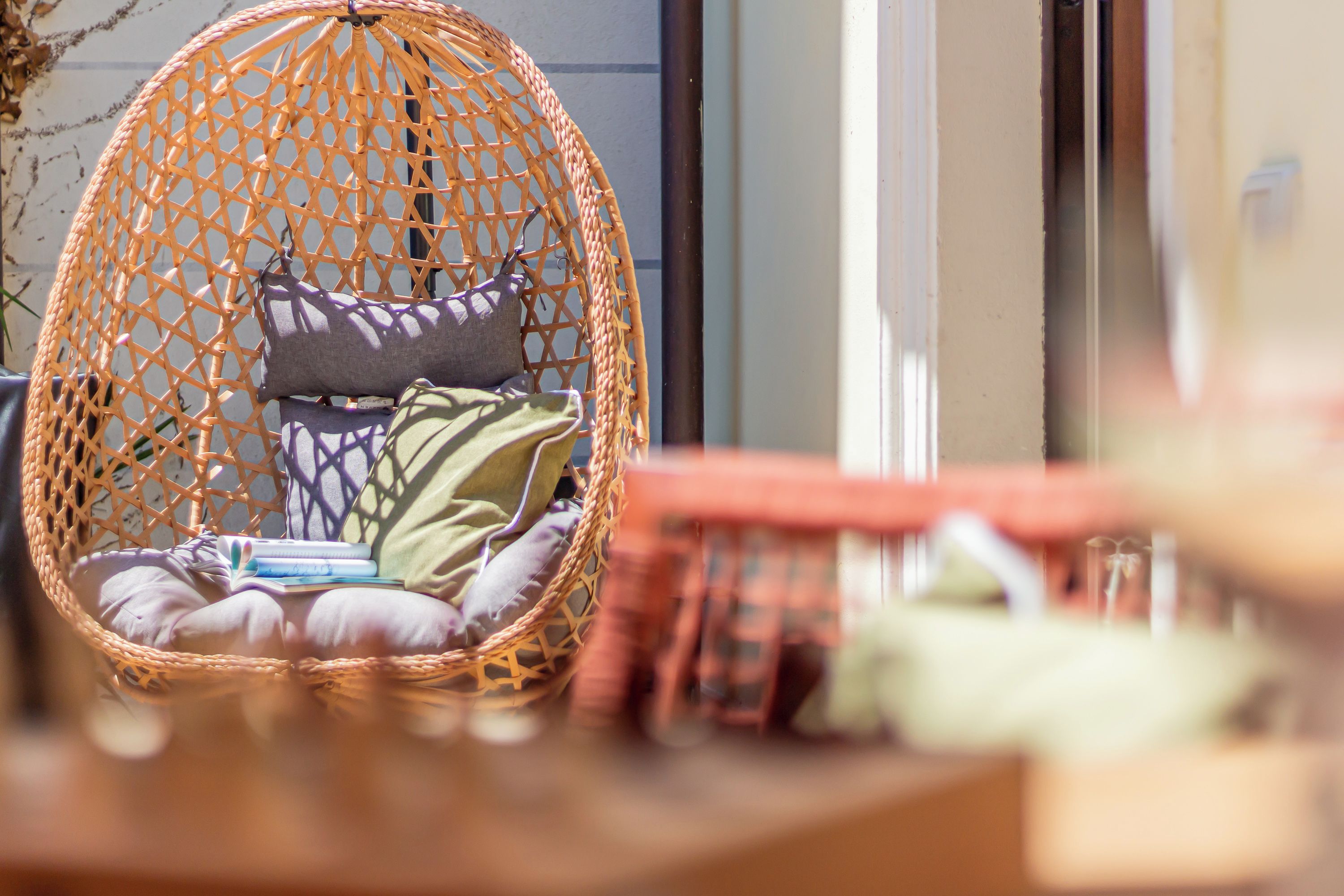 A wicker hanging chair with cushions and books, placed on a wooden table.