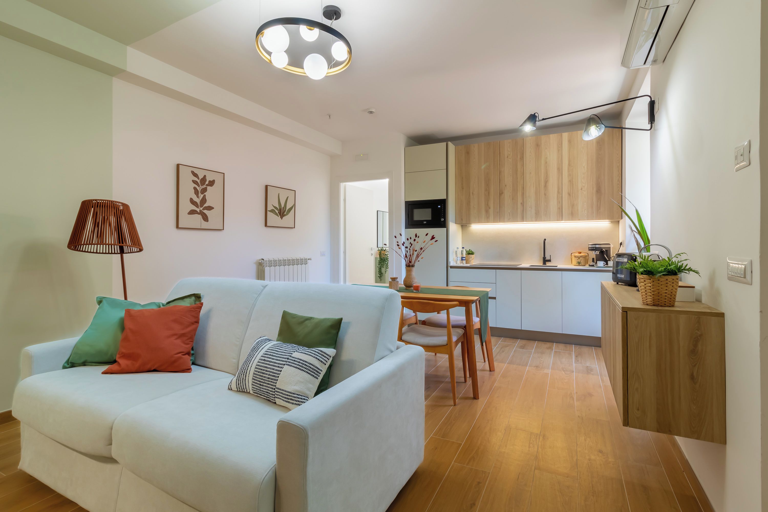 A modern living room with a sofa, a dining table, and a kitchen area with wooden cabinets and a microwave.