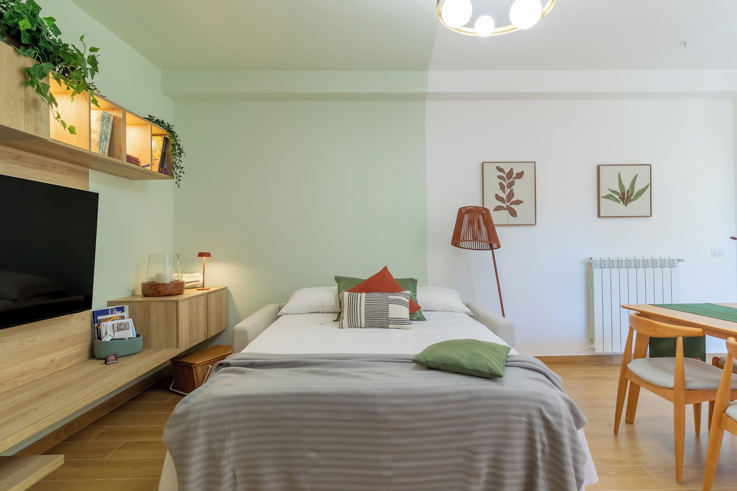 Un dormitorio moderno con cama, mesita de noche, lámpara y televisor.