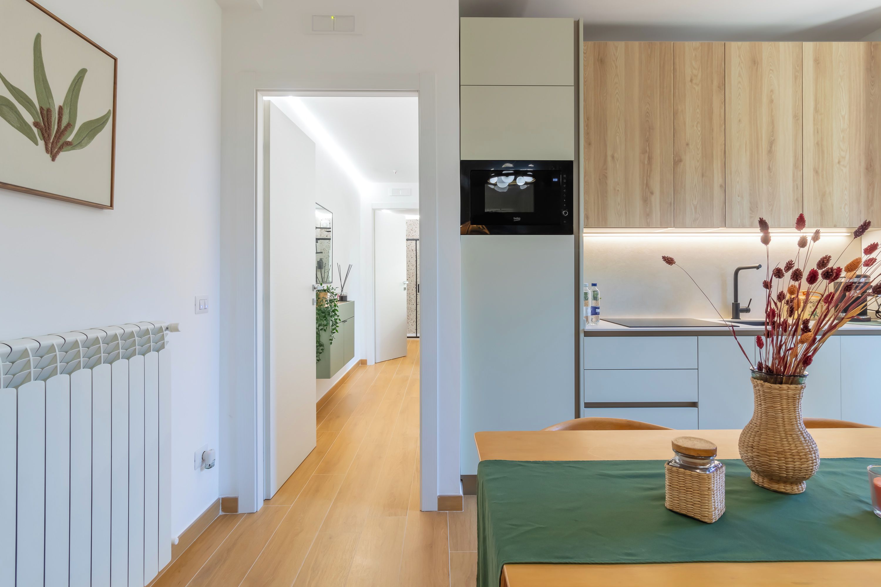 Una cocina moderna con horno empotrado, un comedor con mantel verde y un pasillo que conduce a otra habitación.