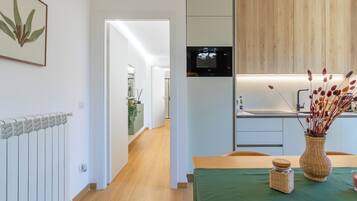 Una cocina moderna con horno empotrado, un comedor con mantel verde y un pasillo que conduce a otra habitación.