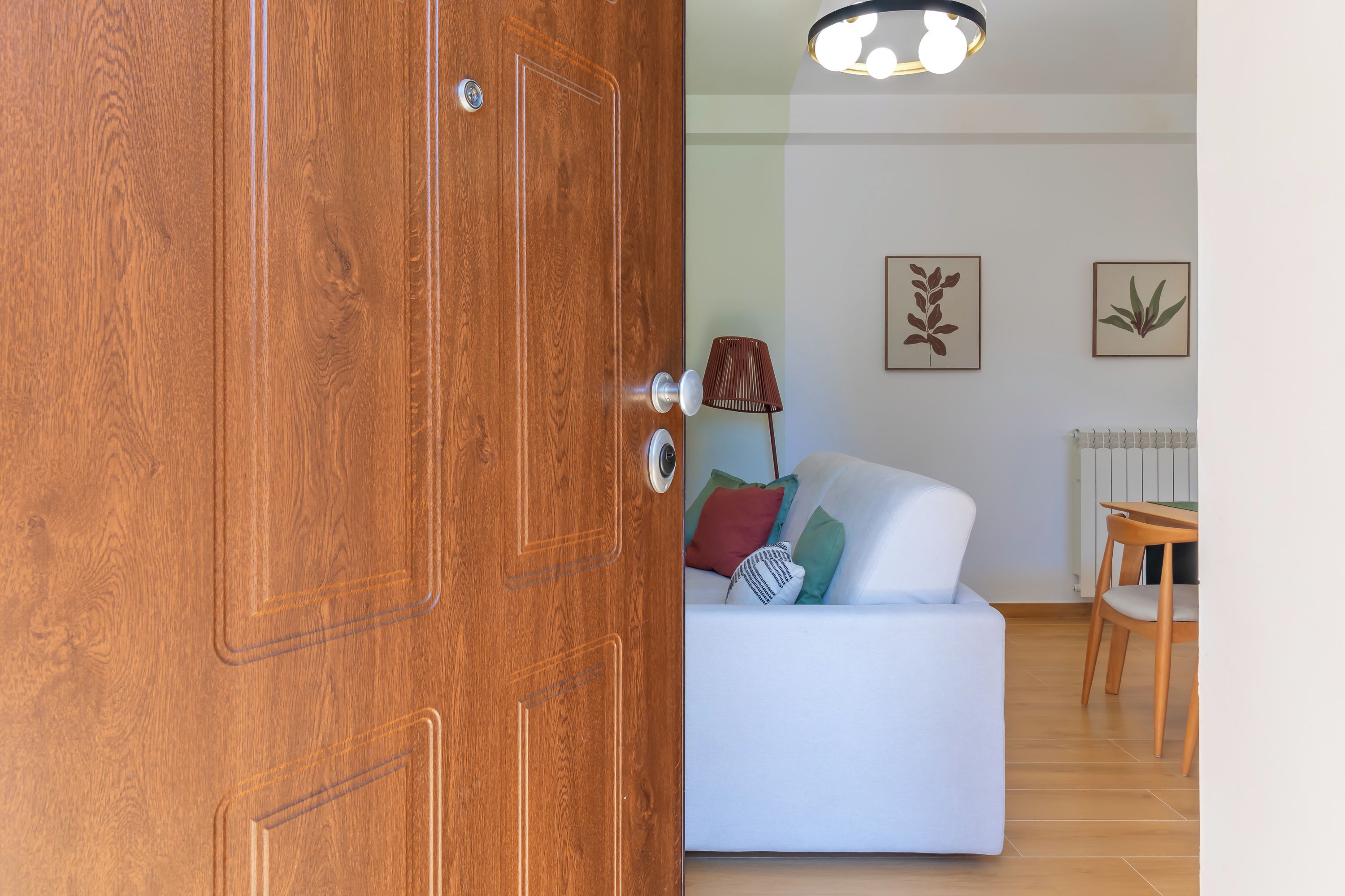 Eine Holztür mit Schlüsselloch, ein weißes Sofa mit Kissen, eine Lampe und gerahmte Wandbilder.