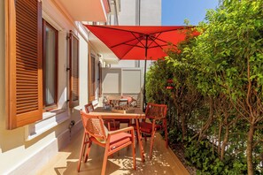 Un patio al aire libre con una mesa, sillas, un paraguas rojo y un seto.
