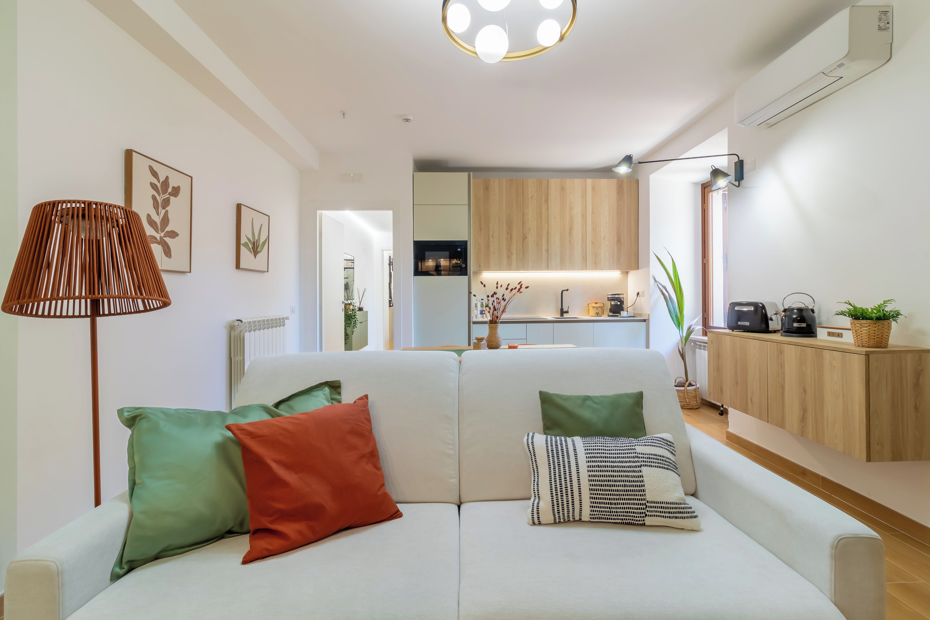A modern living room with a sofa, a lamp, and a kitchen in the background.