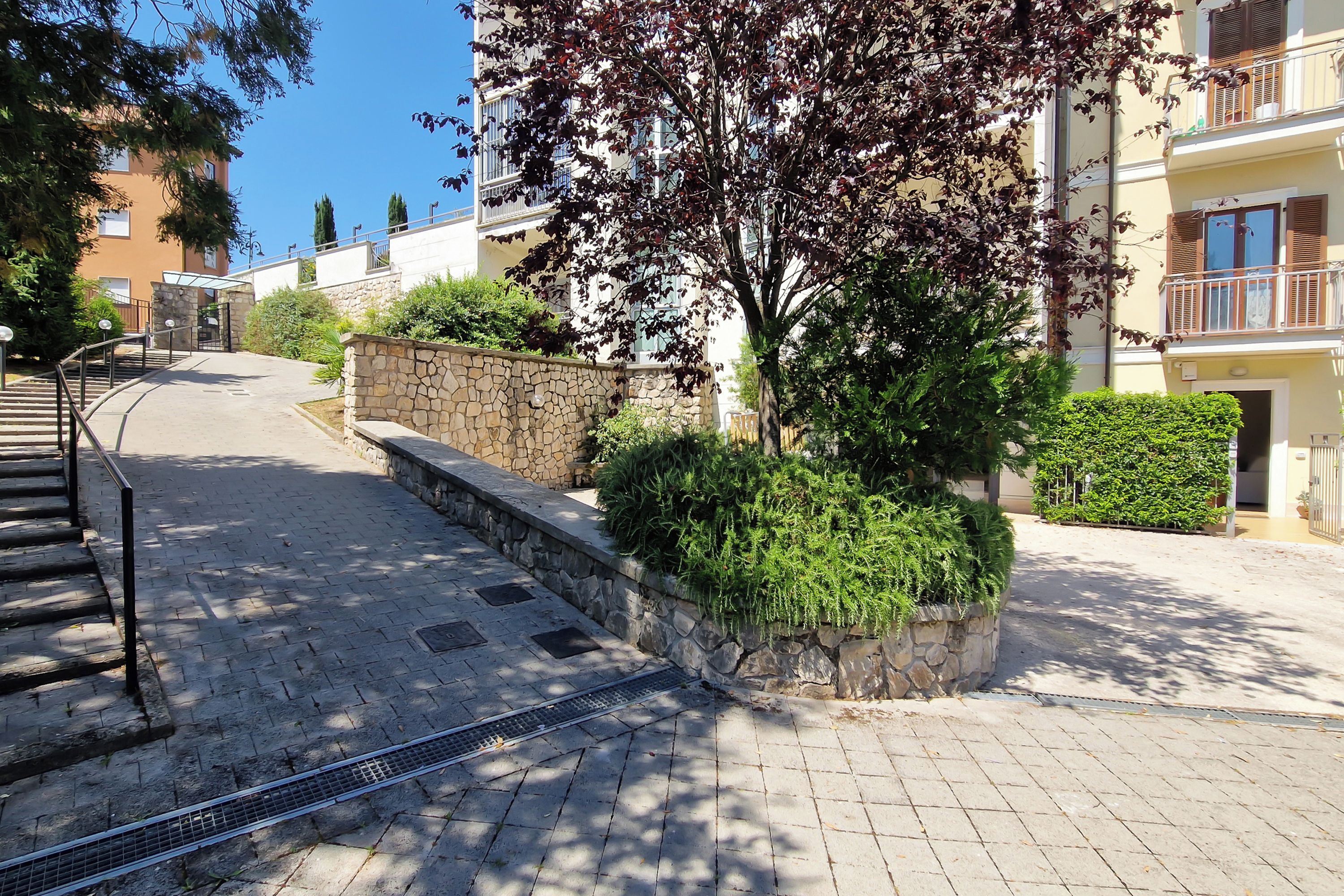 Un camino pavimentado que conduce a un edificio con muros de piedra y vegetación.