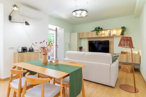 Uma sala de estar moderna com um sofá, uma mesa de jantar com cadeiras, uma televisão e uma máquina de café.