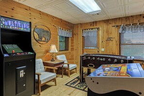 Ein Zimmer mit Holzwänden, einem Kicker, einer Jukebox und zwei Stühlen.