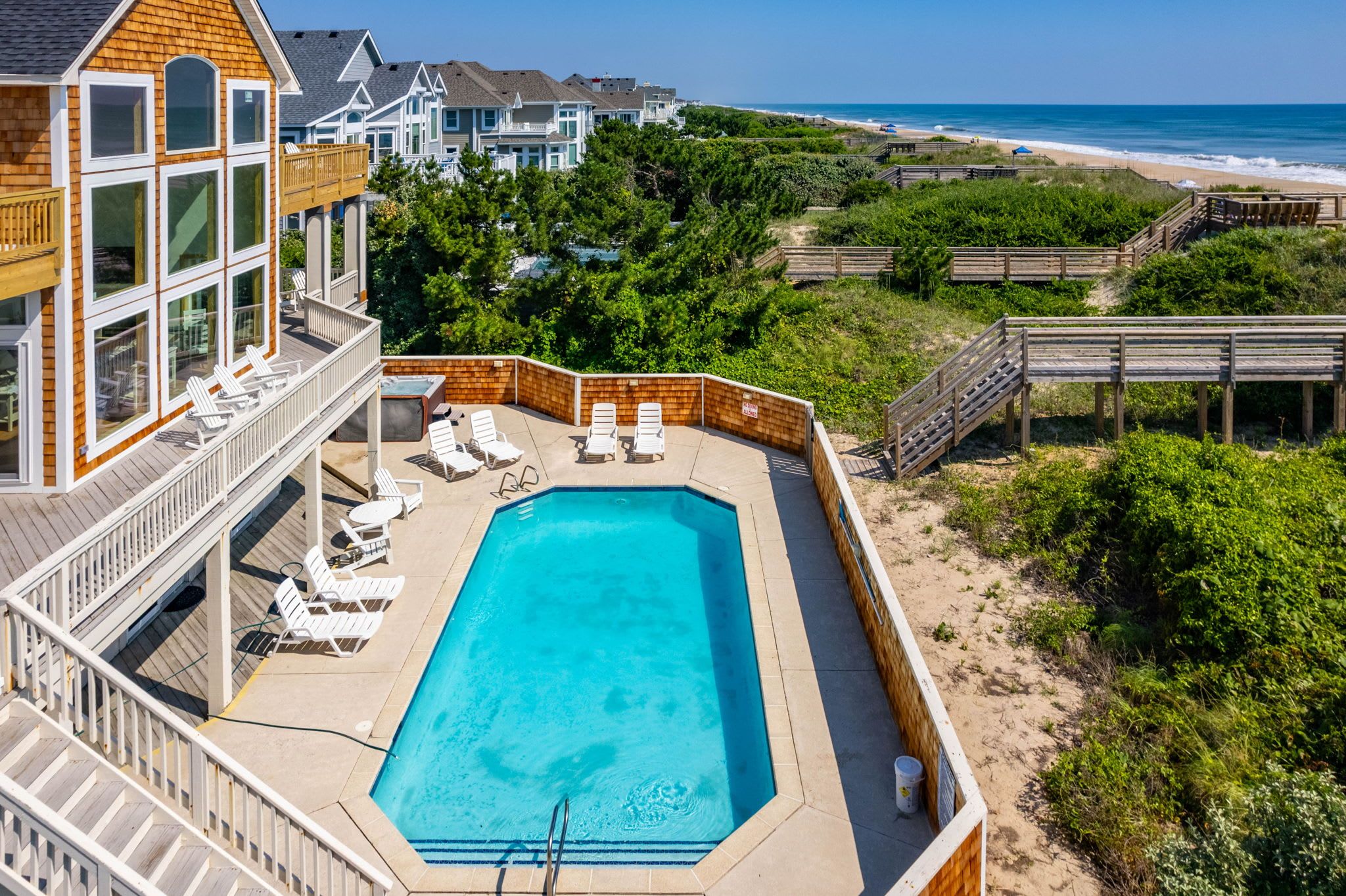A pool with lounge chairs, a wooden deck, and a view of the beach and ocean.
