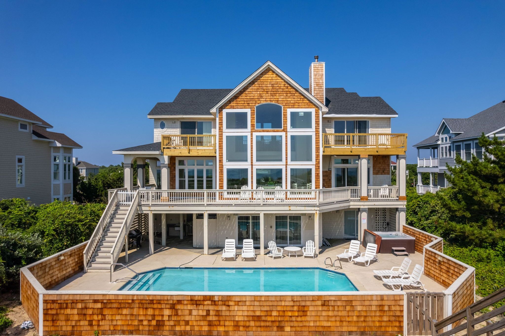 A two-story house with a large deck, a swimming pool, and multiple balconies.