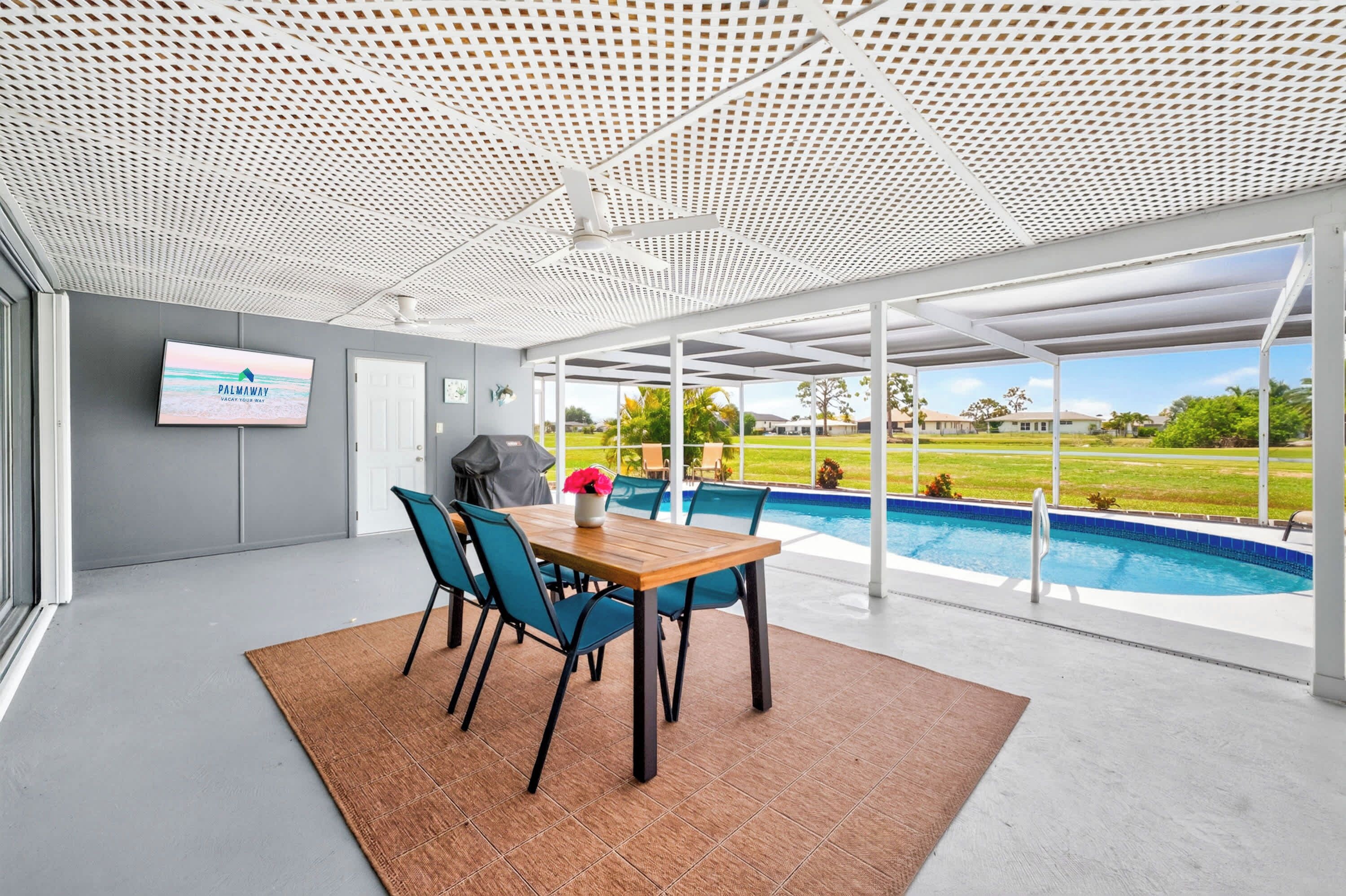 Un área de piscina interior moderna con ventilador de techo, televisión y vista a una piscina exterior.