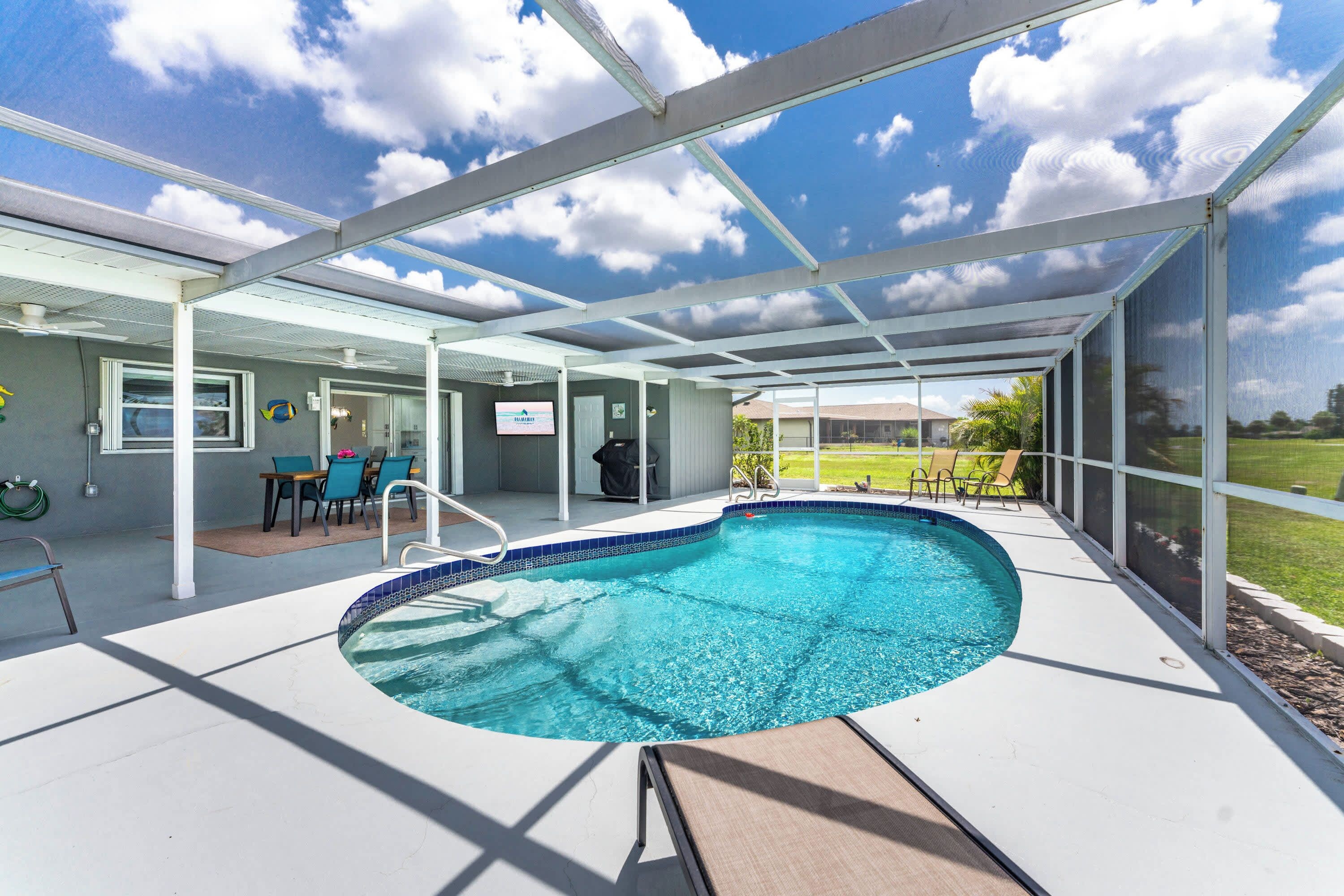 A covered swimming pool with a view of the sky and a grassy area in the background.
