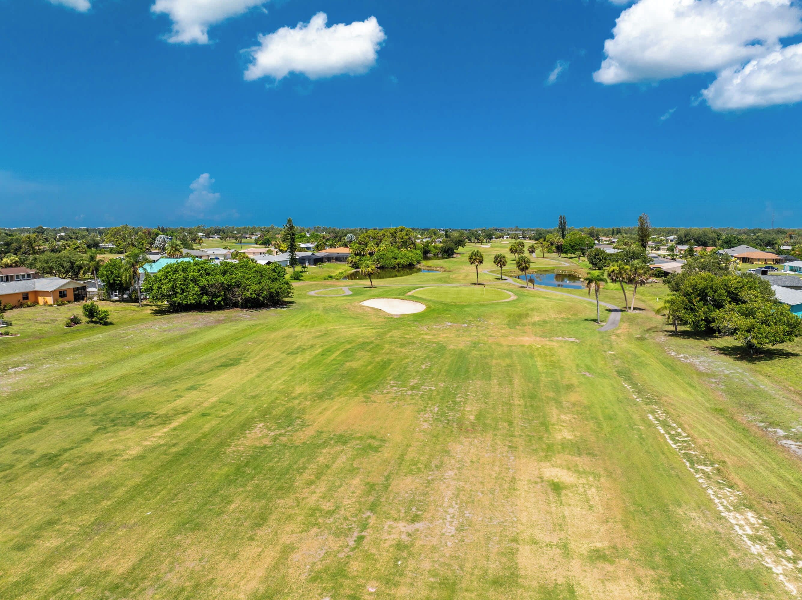 Ein Golfplatz mit blauem Himmel, umgeben von Wohngebäuden und Grünflächen.