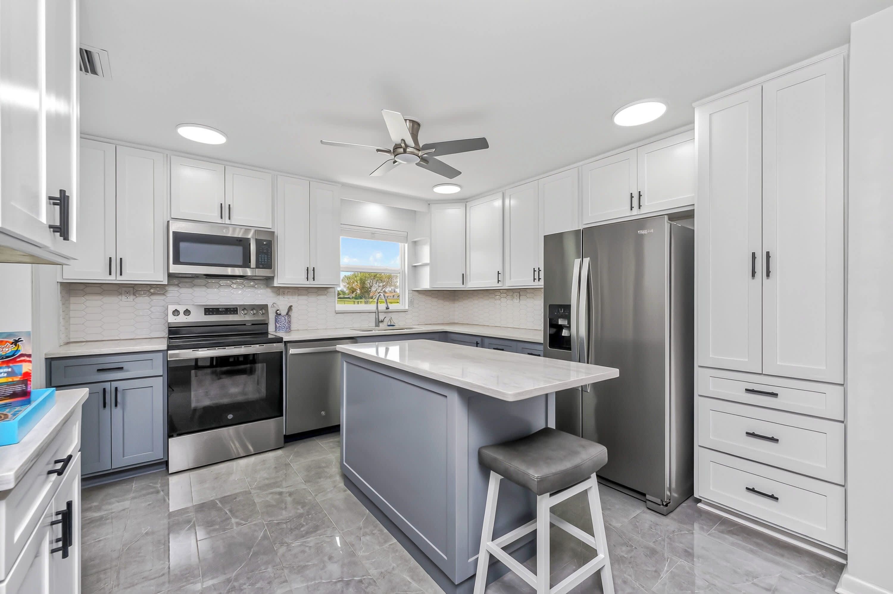 A modern kitchen with white cabinets, stainless steel appliances, a central island, and a ceiling fan.