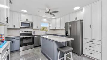 A modern kitchen with white cabinets, stainless steel appliances, a central island, and a ceiling fan.