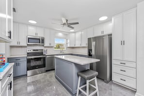A modern kitchen with white cabinets, stainless steel appliances, a central island, and a ceiling fan. - Best Deal in Rotonda - Sleeps 8, Pool, Golf, Fun! (Rotonda West)