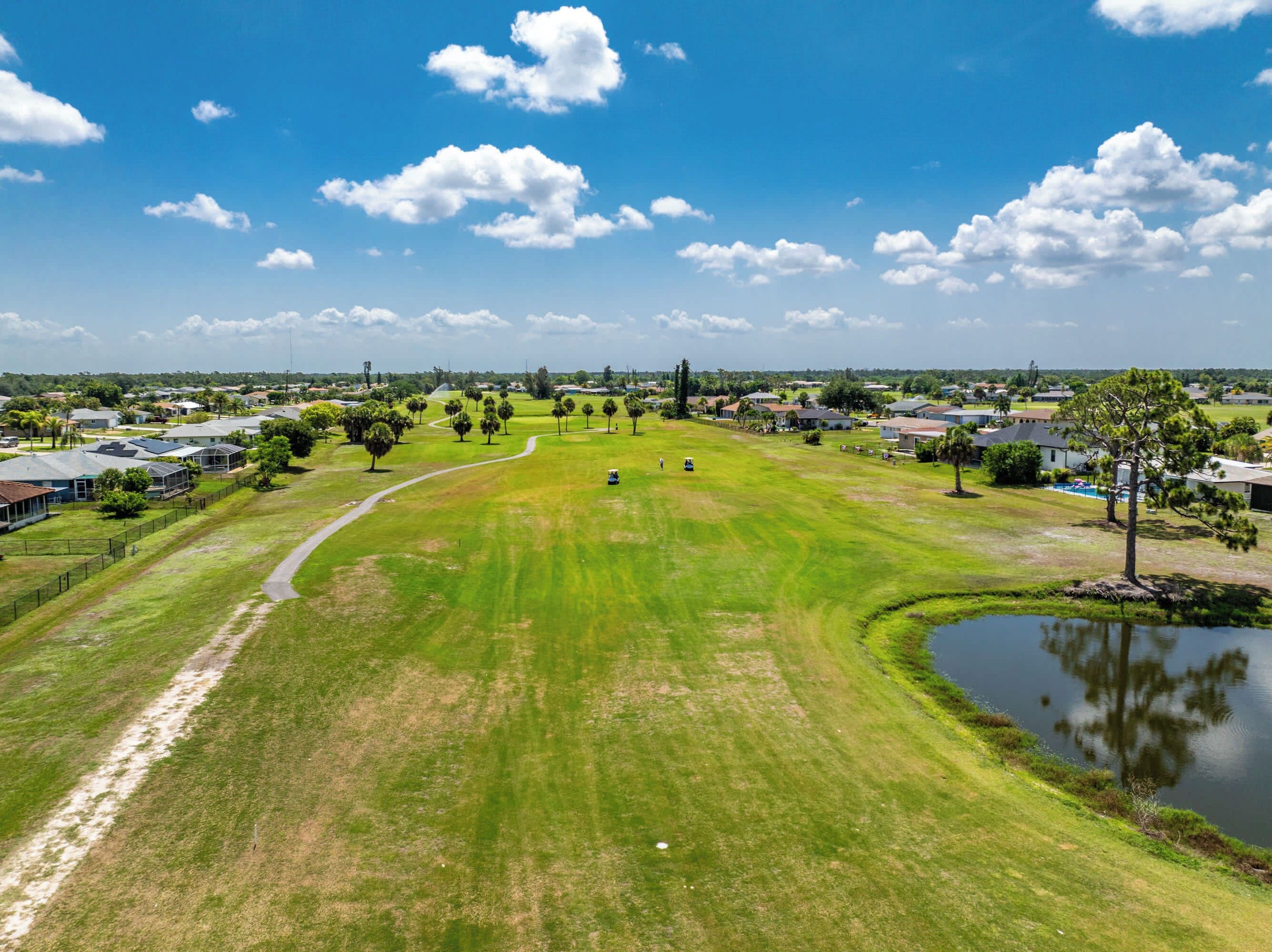 A golf course with a pond, houses, and a clear sky.