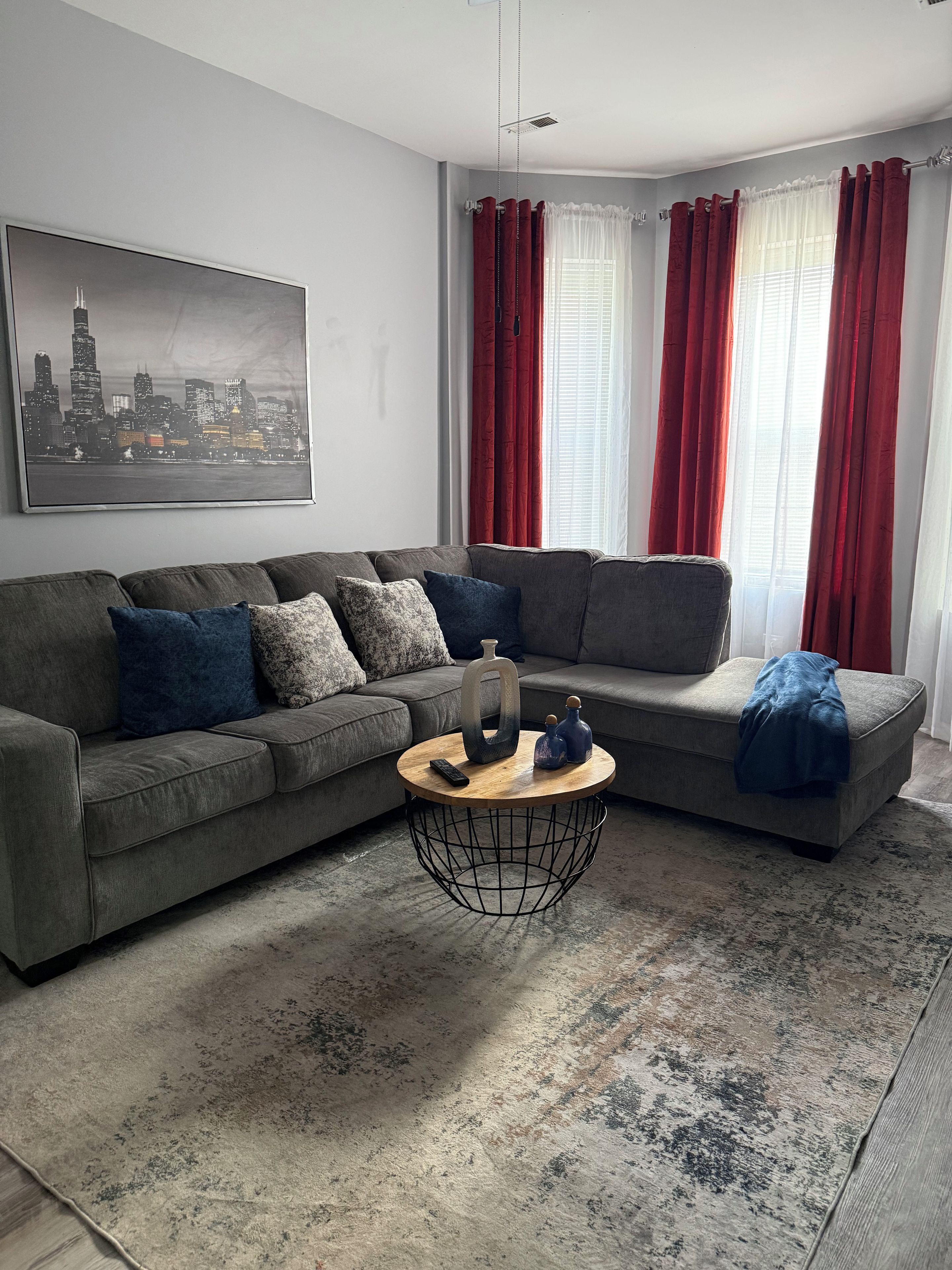 Una sala de estar moderna con un sofá seccional gris, una mesa redonda de centro y una pintura de un paisaje urbano en la pared.