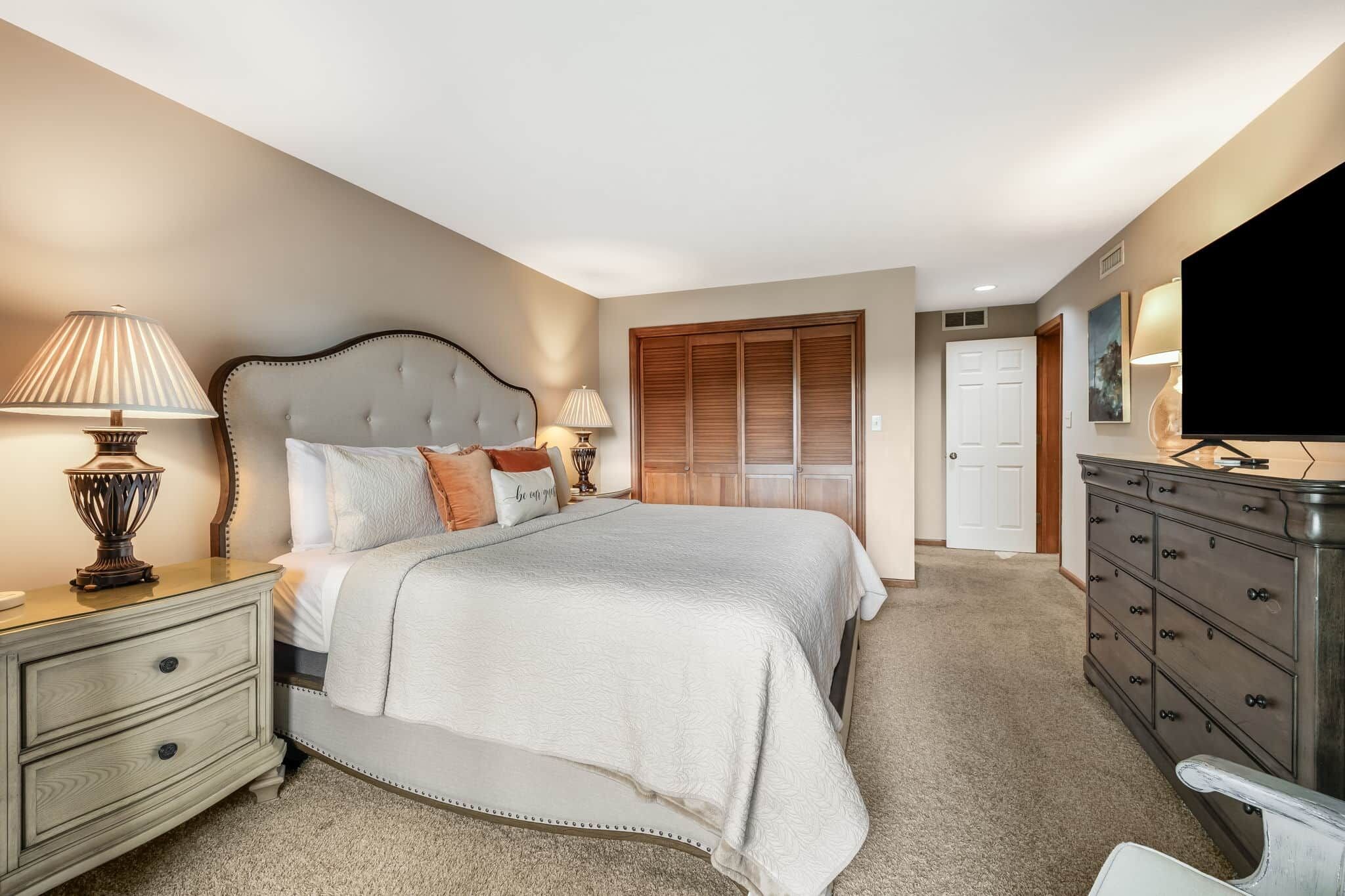 Une chambre à coucher comprenant un lit, des tables de chevet, une commode, un téléviseur et un placard.