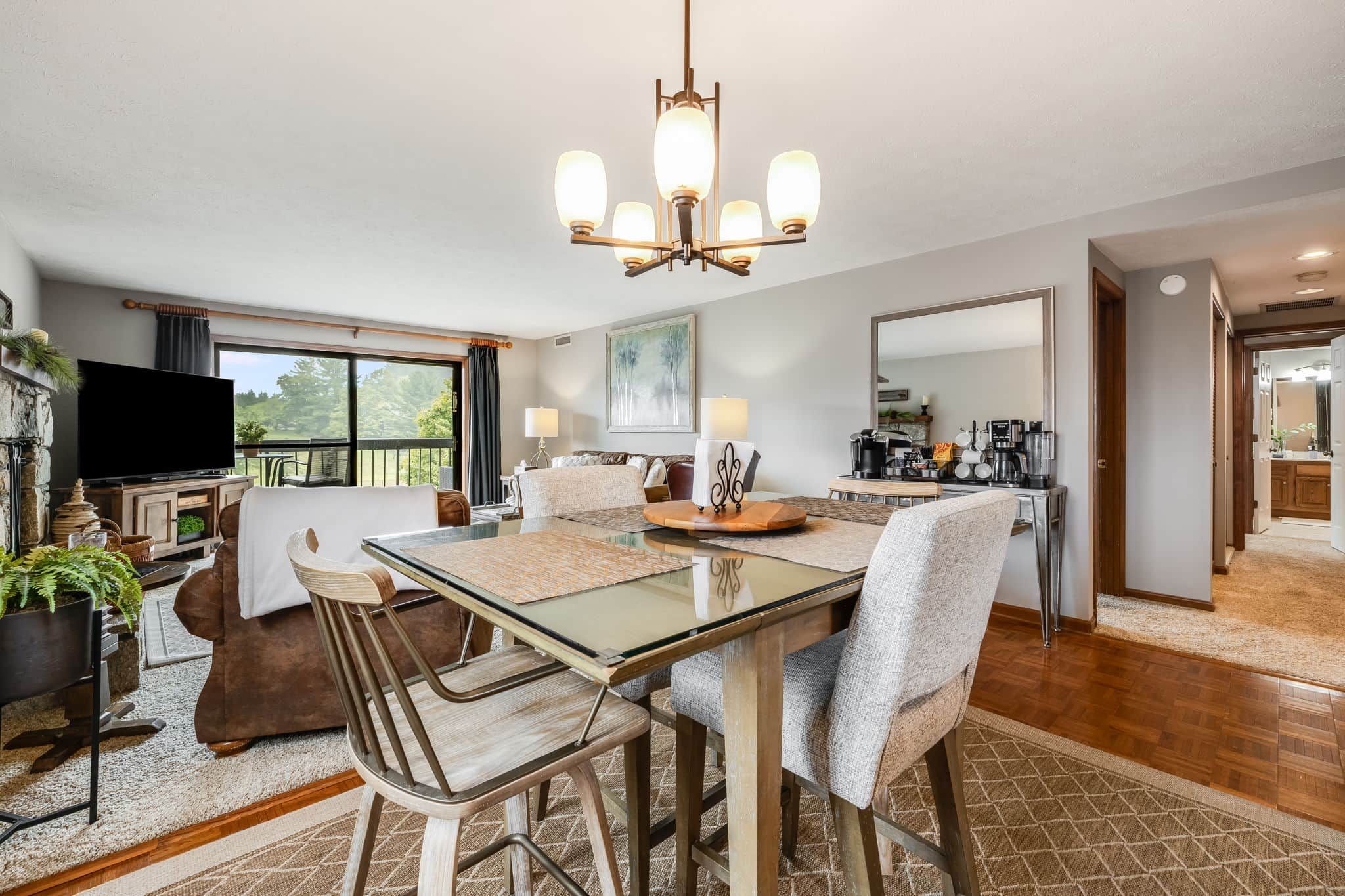 A modern living room with a glass dining table, comfortable seating, a television, and a fireplace.