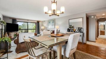 A modern living room with a glass dining table, comfortable seating, a television, and a fireplace.