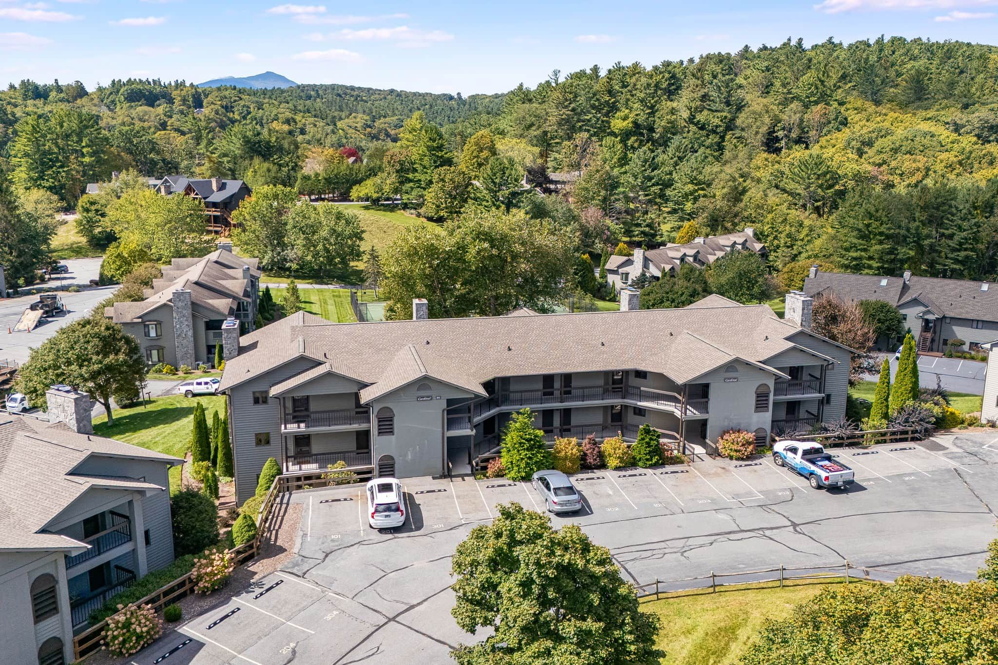 A multi-story hotel with a parking lot, surrounded by greenery and hills.
