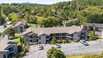 A multi-story hotel with a parking lot, surrounded by greenery and hills.