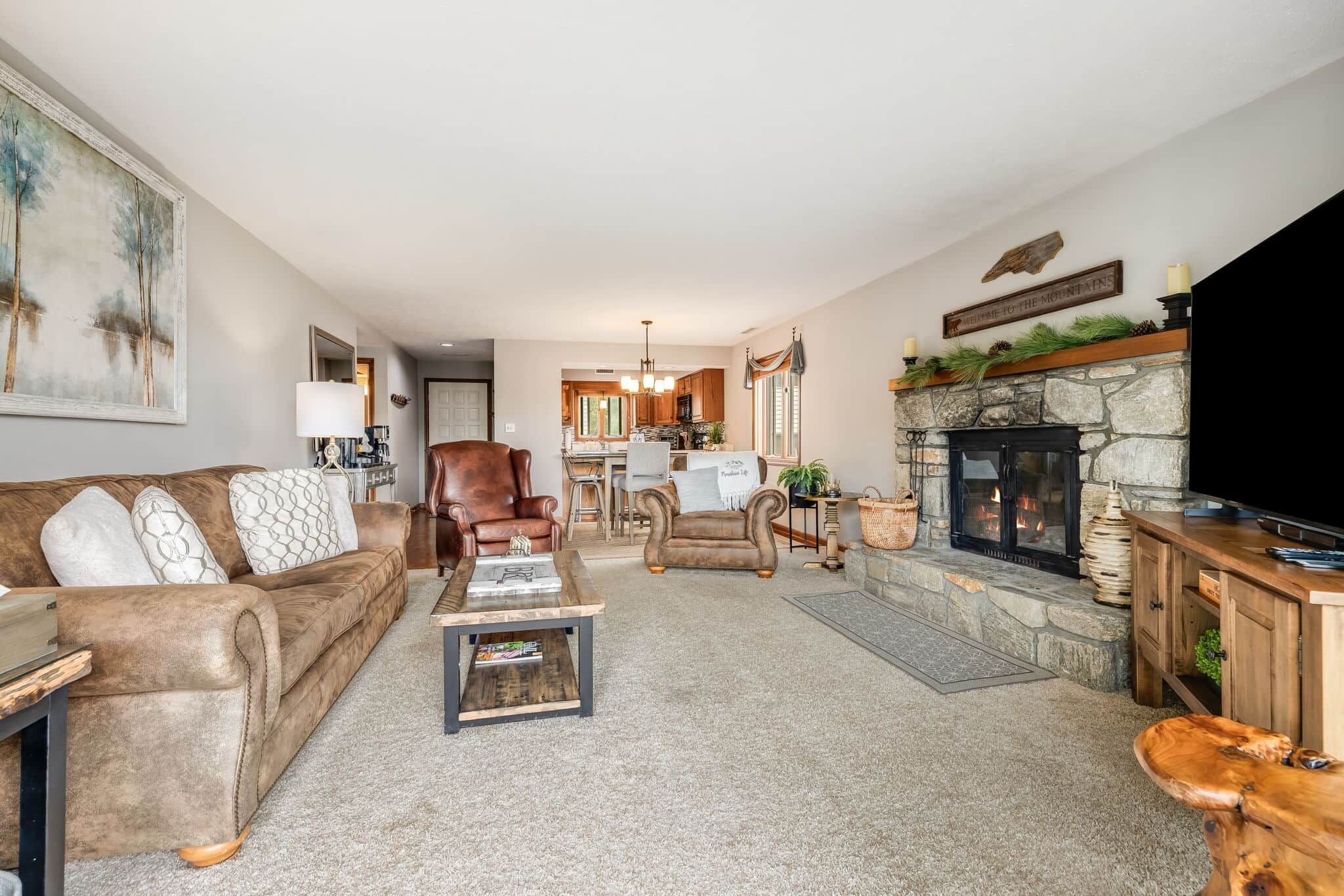 A living room with a fireplace, a television, and a kitchen in the background.