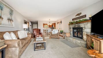 A living room with a fireplace, a television, and a kitchen in the background.