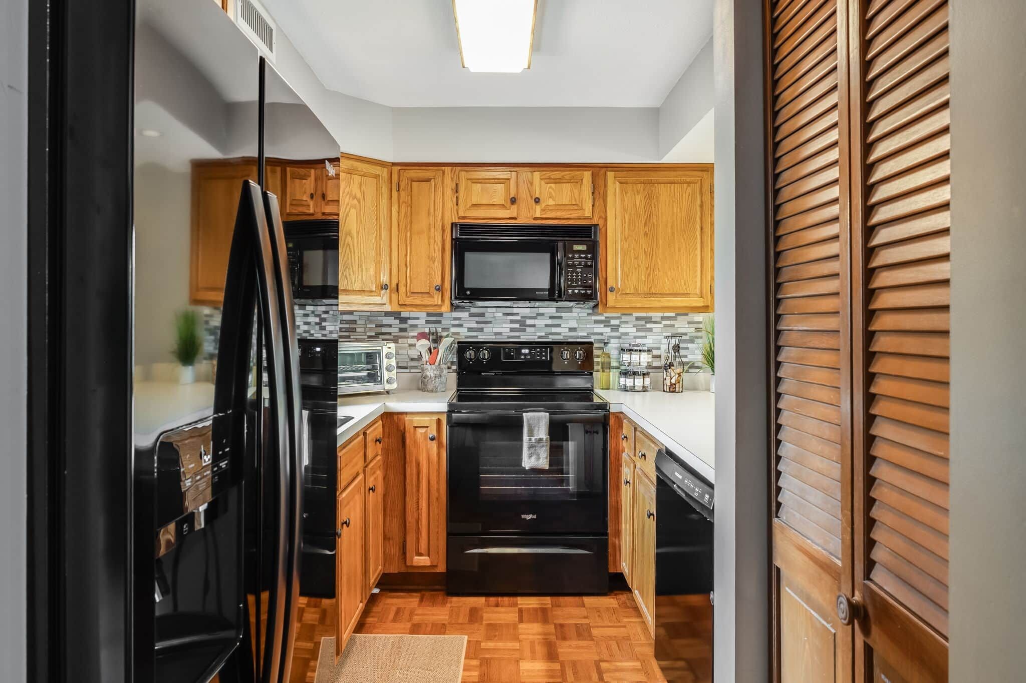 A kitchen with wooden cabinets, a black microwave, a stove, and a dishwasher.