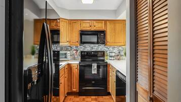 A kitchen with wooden cabinets, a black microwave, a stove, and a dishwasher.