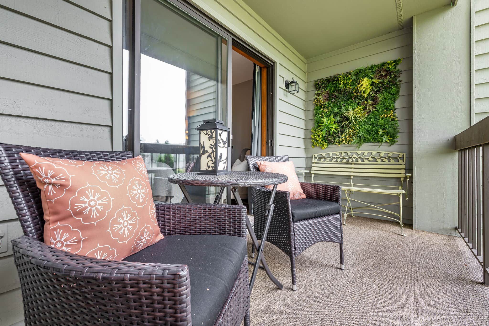 A balcony with wicker furniture, a small table, and a green wall with plants.