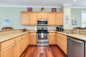 A kitchen with wooden cabinets, stainless steel appliances, granite countertops, and a dishwasher. - Reef House Islamorada | Beach • Pool • Marina (Islamorada)