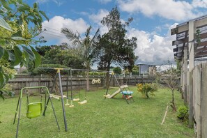 A backyard with a swing set, a slide, and a small tree. - Cozy Family Home - Manukau City Holiday Home (Manurewa East)