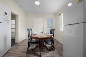 Un coin repas comprenant une table ronde, quatre chaises, un réfrigérateur et une porte avec une pancarte.