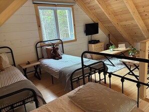 A cozy attic bedroom with a bed, a desk, and a window overlooking a forest. - Lovely off grid chalet in Saint-Cyrille-de-Lessard awaits you (Saint-Cyrille-de-Lessard)