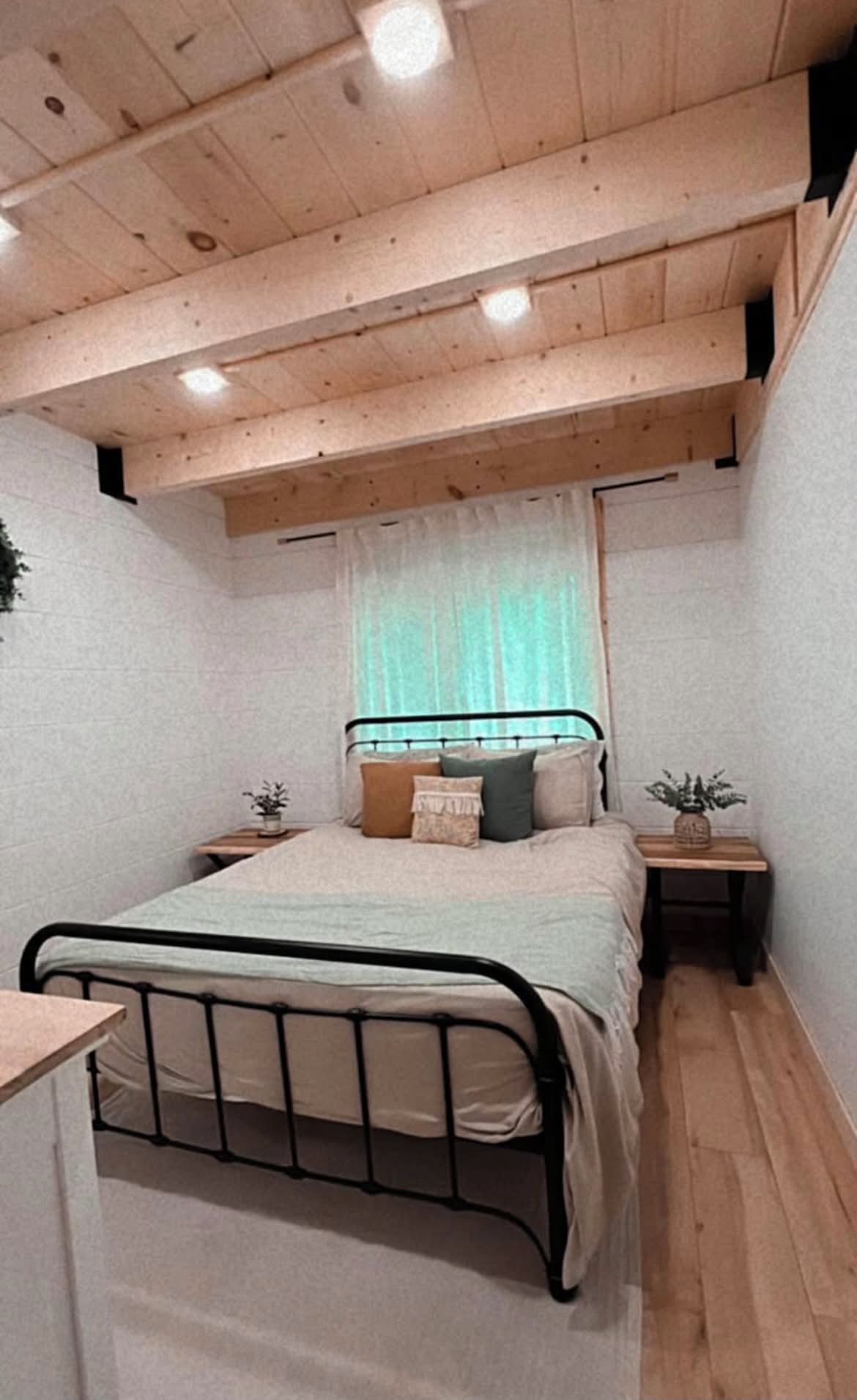 A bedroom with a metal bed frame, a wooden ceiling, and a small bedside table with a plant.