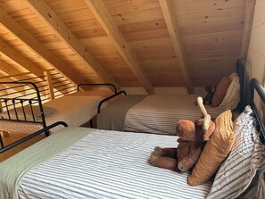 A dormitory room with two bunk beds, wooden beams on the ceiling, and a stuffed toy on one bed.