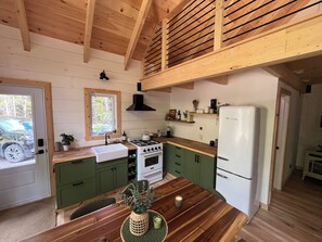 A kitchen with wooden beams, a stove, a sink, and a refrigerator. - Lovely off grid chalet in Saint-Cyrille-de-Lessard awaits you (Saint-Cyrille-de-Lessard)