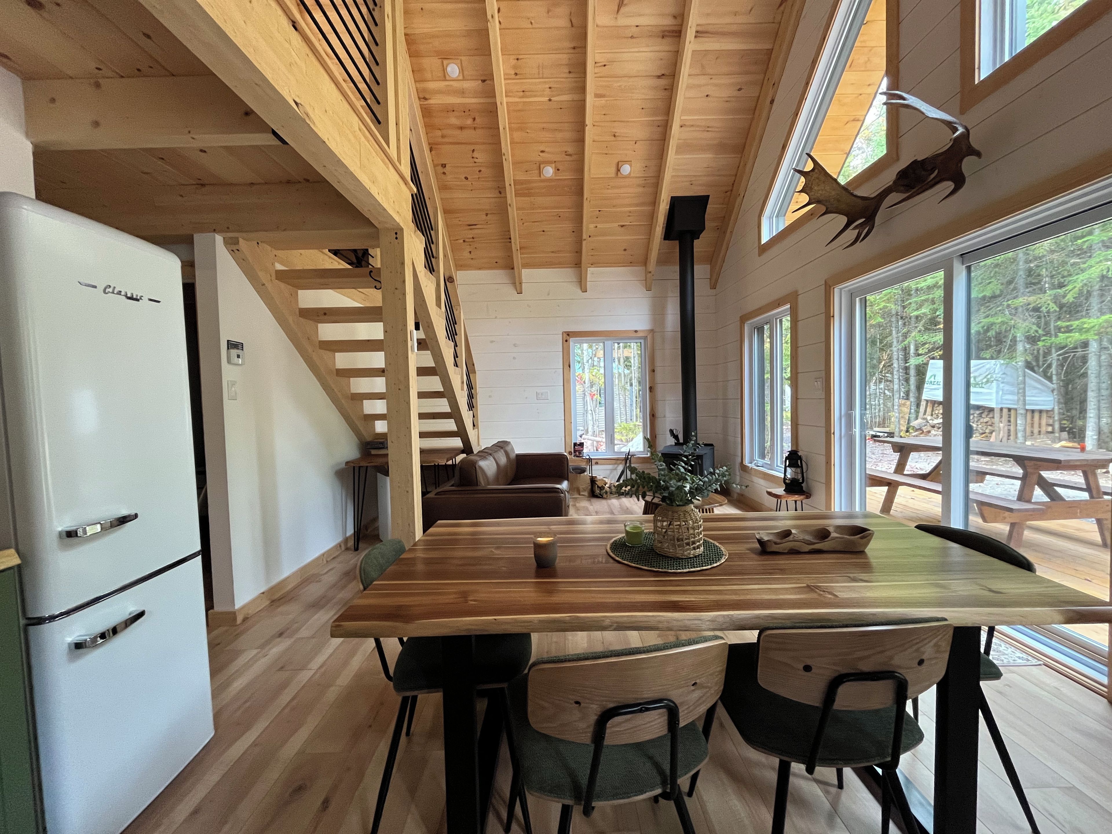 A wooden interior with a dining table, chairs, a sofa, and a kitchen area with a refrigerator.