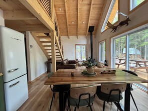 A wooden interior with a dining table, chairs, a sofa, and a kitchen area with a refrigerator. - Lovely off grid chalet in Saint-Cyrille-de-Lessard awaits you (Saint-Cyrille-de-Lessard)