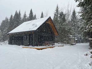 A cabin with a wooden exterior, a porch, and a snow-covered roof.