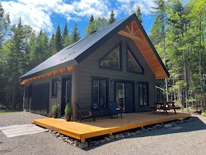 A cabin with a large deck, multiple windows, and a sloped roof.