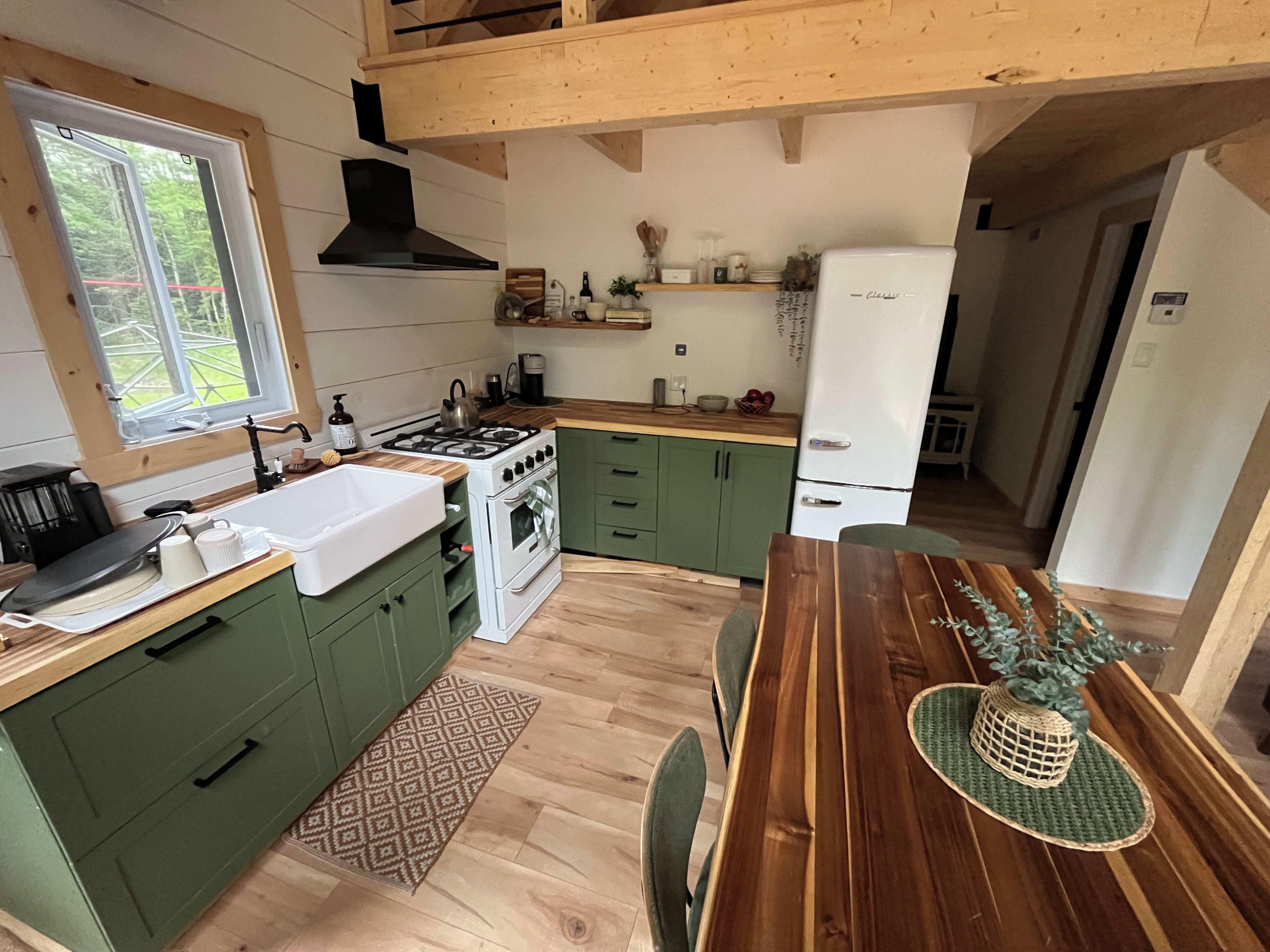 A modern kitchen with green cabinets, a wooden dining table, and a built-in stove.
