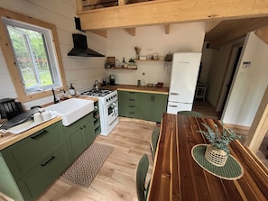 A modern kitchen with green cabinets, a wooden dining table, and a built-in stove.