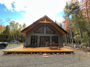 A cabin with a wooden deck, large windows, and a stone foundation.