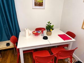 A room with a white table, red chairs, a small plant, a basket, and a roll of paper towels. - ESCALE DE LA BREGERE (Limoges)