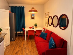 A compact living space with a kitchenette, a dining area, and a red sofa with blue cushions. - ESCALE DE LA BREGERE (Limoges)