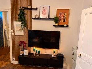 A modern living room with a flat-screen TV mounted on a black entertainment unit, surrounded by decorative items and wall art. - ESCALE DE LA BREGERE (Limoges)